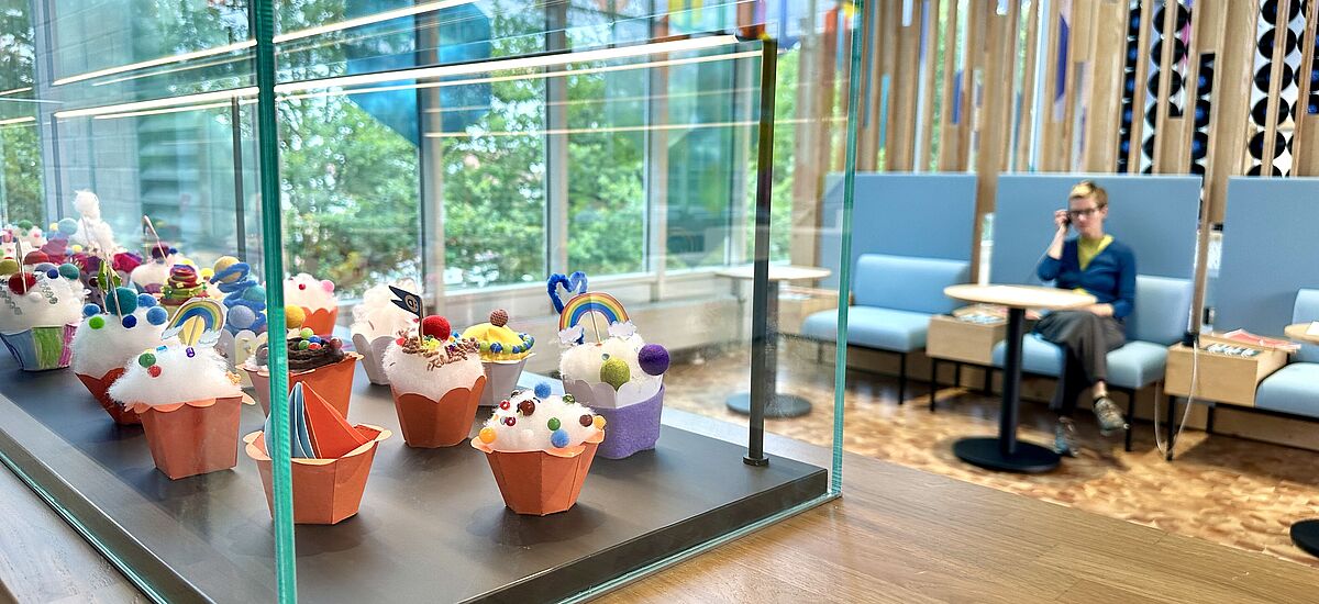 Blick in den "Café"-Bereich Eine Vitrine gefüllt mit gebastelten Cupcakes in der Ausstellung Dienstleistung in der DASA