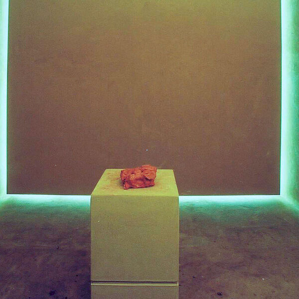 Ausstellungsraum mit Podest in der Mitte auf dem ein roter Lehmklumpen positioniert ist.