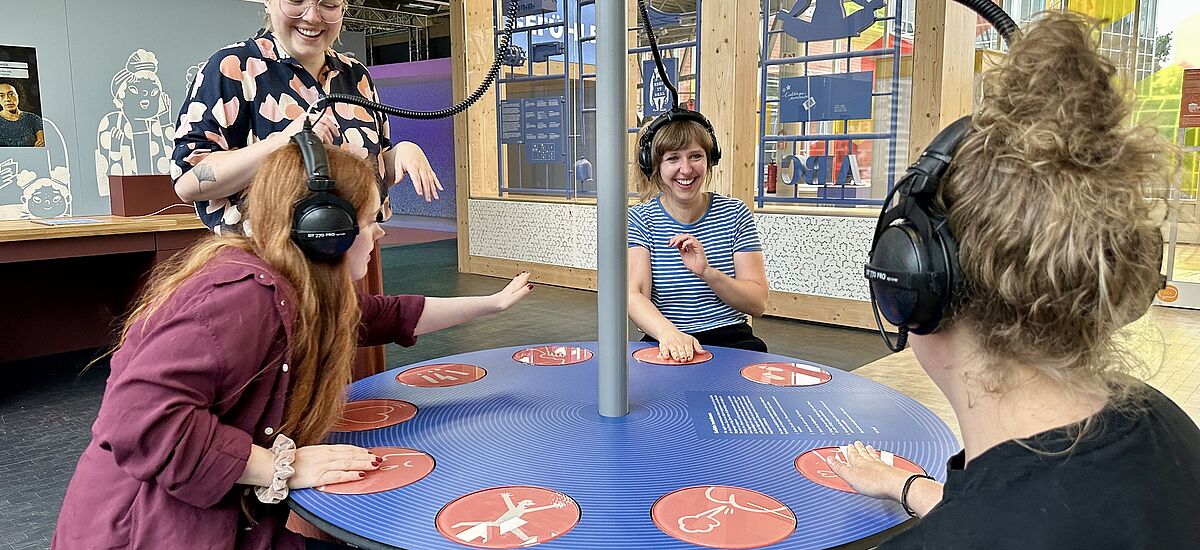 Emo-Tisch Vier Frauen sitzen um einen interaktiven Tisch in der Ausstellung Dienstleistung in der DASA und spielen zusammen.