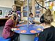 Vier Frauen sitzen um einen interaktiven Tisch in der Ausstellung Dienstleistung in der DASA und spielen zusammen.