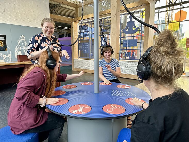 Vier Frauen sitzen um einen interaktiven Tisch in der Ausstellung Dienstleistung in der DASA und spielen zusammen.