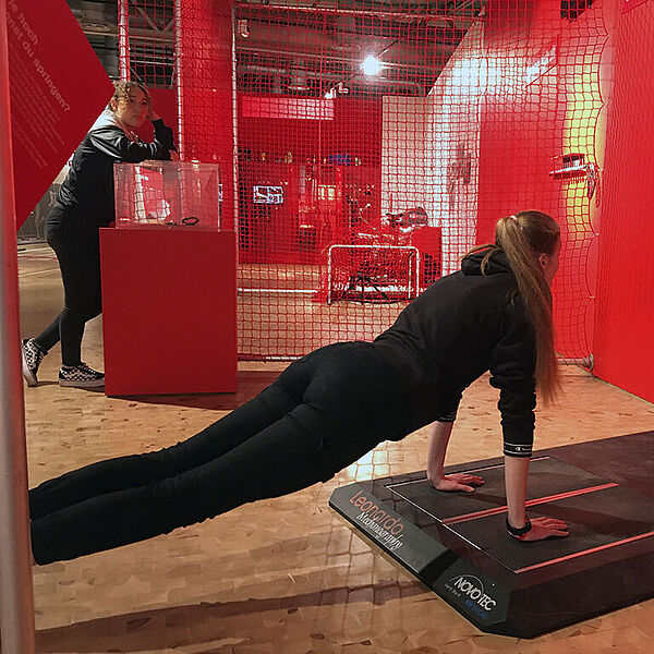 Junge Frau macht Liegestütze an einer eine Sportstation in einer DASA Ausstellung