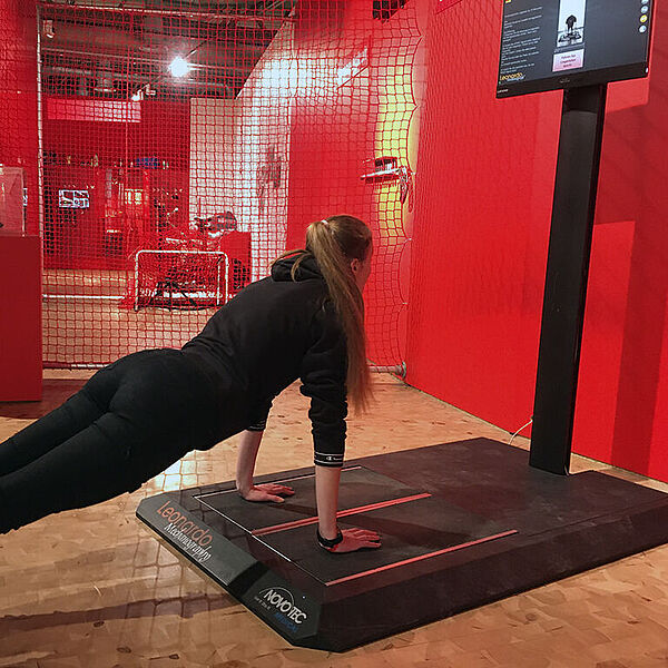 Junge Frau macht Liegestütze an einer eine Sportstation in einer DASA Ausstellung