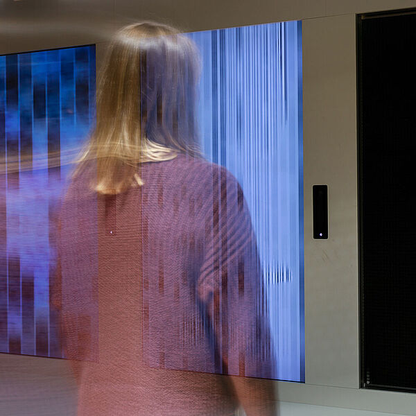 Junge Frau betrachtet ein digitales Kunstwerk in der Ausstellung Neue Medien