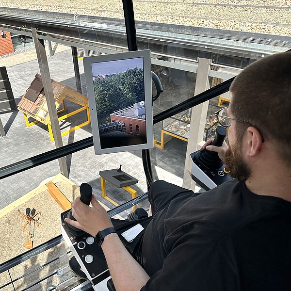 Mann sitzt in einer Krankabine und steuert eine Kamera in der DASA-Ausstellung Hochbau