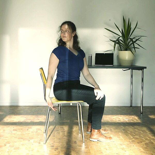 Eine Frau sitzt auf einem Bürostuhl und macht Gymnastikübungen.