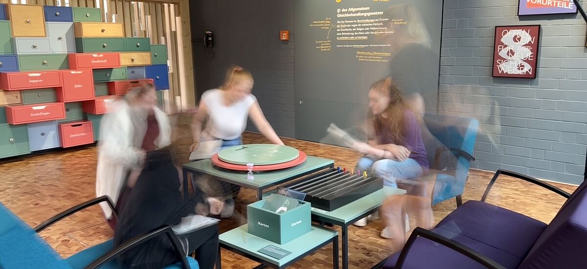 Privilegien-Spiel Eine Gruppe Jugendlicher sitzt um einen interaktiven Tisch in der Ausstellung "Dienstleistung" in der DASA und spielt jeweils fiktive Biografien nach.