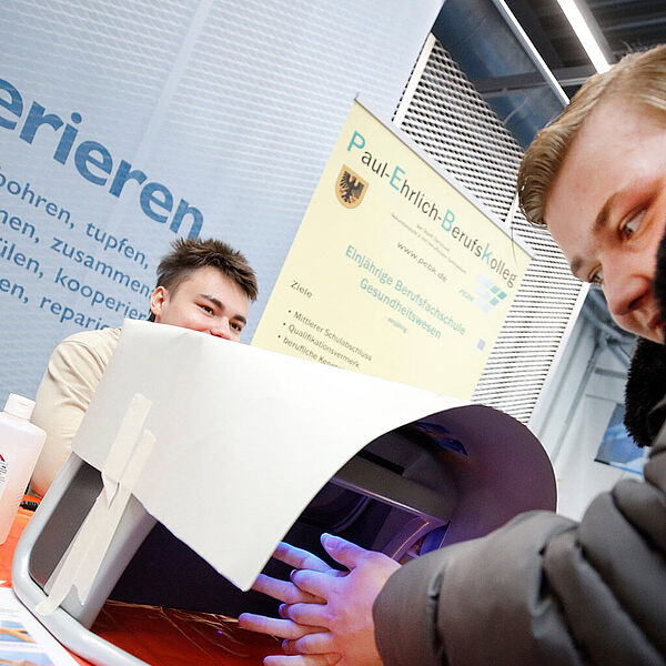 Junger Mann probiert an einem Stand eine Mitmachaktion zur Handdesinfektion aus