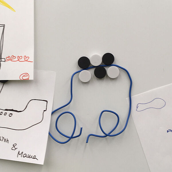 Formen aus Draht liegen auf Bildern, die von Kindern gemalt wurden.