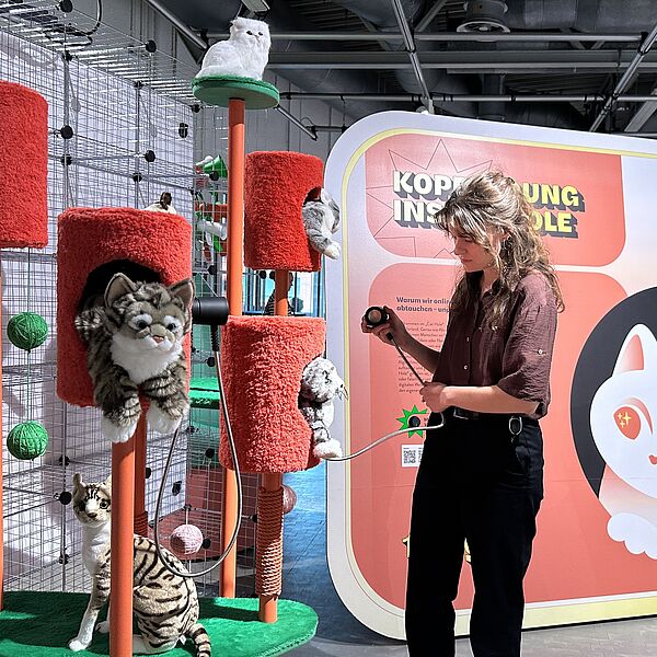 Besucherin vor einem Kratzbaum für Katzen in der Ausstellung "Alles im Angebot".