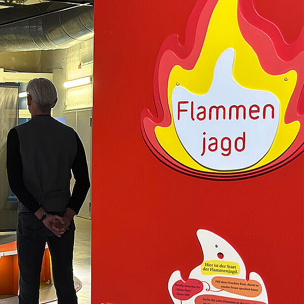 Blick auf eine Stele, an der sich eine ausgesägte Flamme aus Holz befindet und das Wort Flammenjagd steht